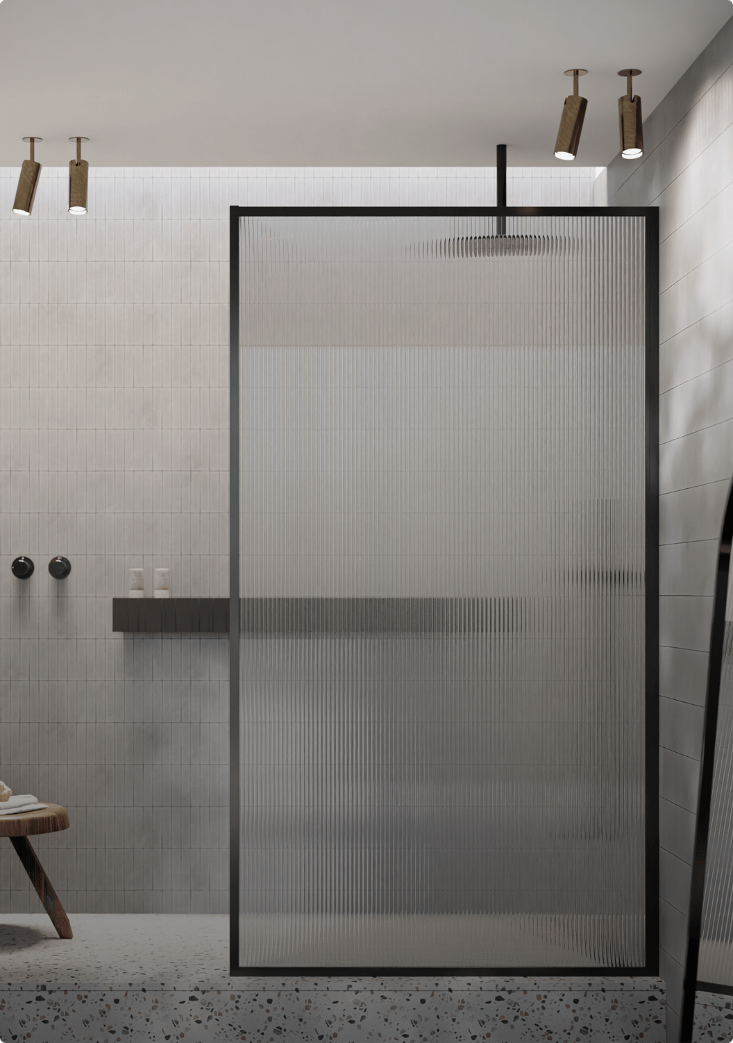 Douche à l’italienne moderne d’une salle de bains x²o, posée sur une plateforme en terrazzo, avec des carreaux muraux gris clair posés à la verticale et une paroi de douche en verre nervuré encadrée de noir. Un petit tabouret en bois avec une serviette est visible à gauche, et un grand miroir debout à droite.