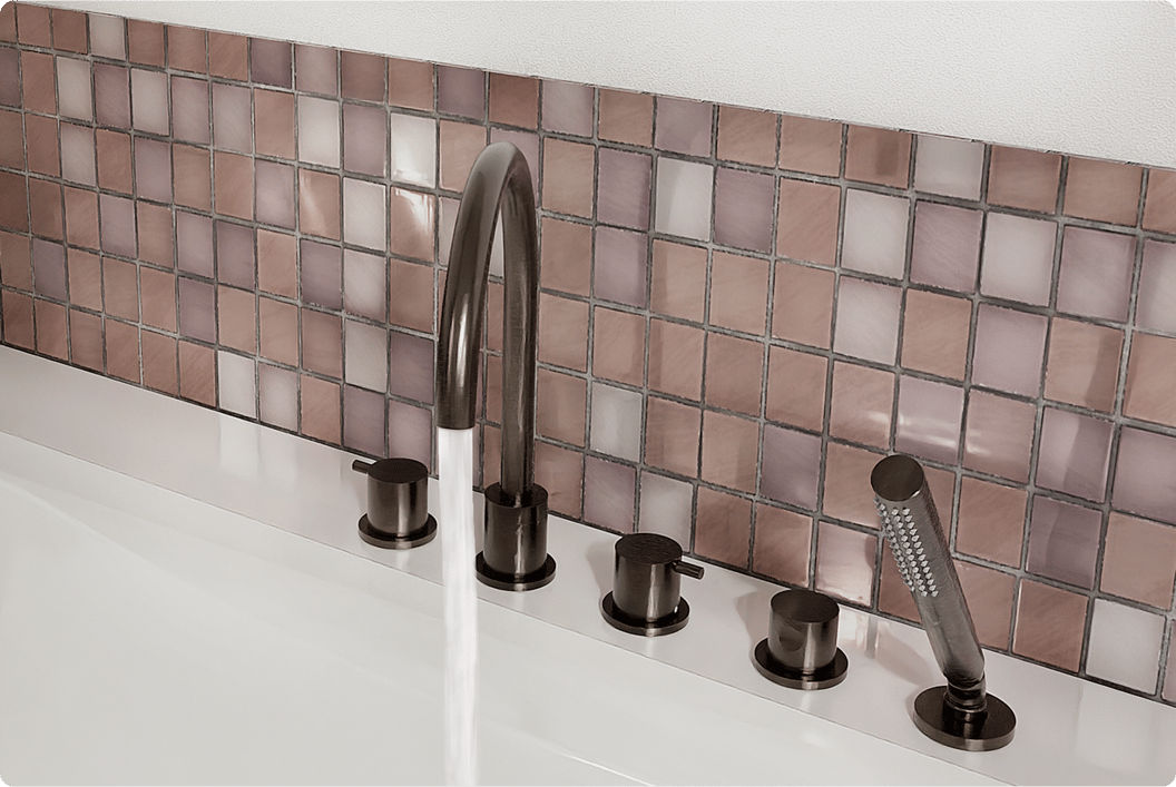 Detail van een badrand met elegante bronzen mengkranen, handdouche en sierlijke mozaïektegels in zachte roze en paarse tinten. Een luxueuze afwerking met metallic accenten in x²o badkamers.