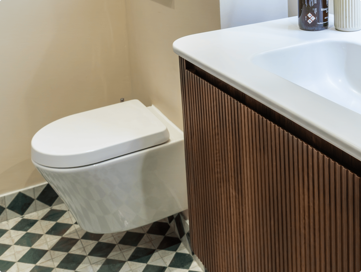 Moderne hangtoilet van x²o badkamers naast een houten geribbeld wastafelmeubel met wit wastafelblad, geplaatst op een vloer met zwart-wit-groen geometrisch patroon in een hedendaagse badkamer met lichte muren