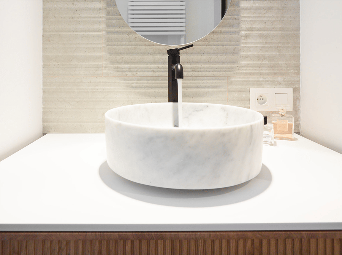 Lavabo en marbre avec robinet noir, miroir rond et accessoires.