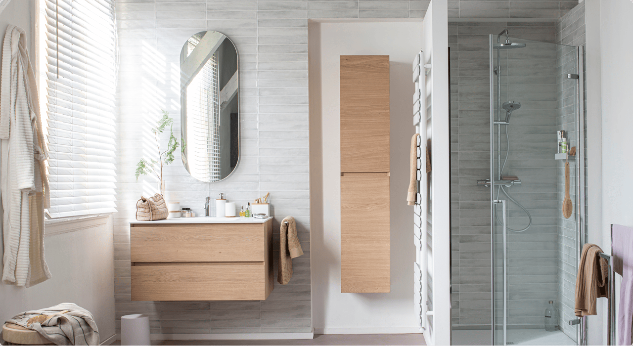 Salle de bains moderne avec meubles en bois, miroir ovale et douche vitrée, chez X2O salles de bains.