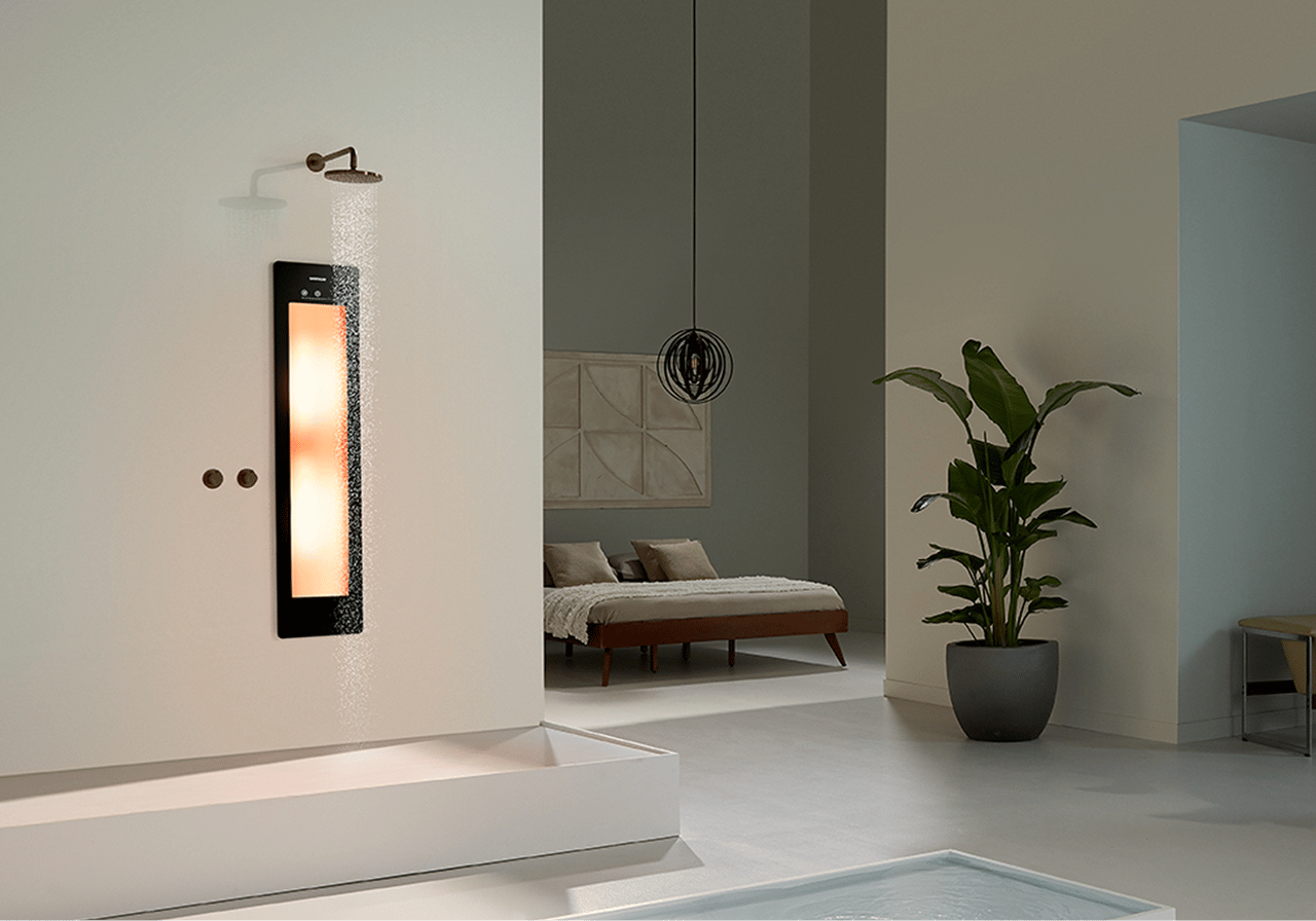 Ruime badkamer met een Sunshower-paneel dat warm licht geeft, ingebouwd in de douchewand. Naast de douche staat een grote groene plant en op de achtergrond een slaapkamer met een laag bed. 