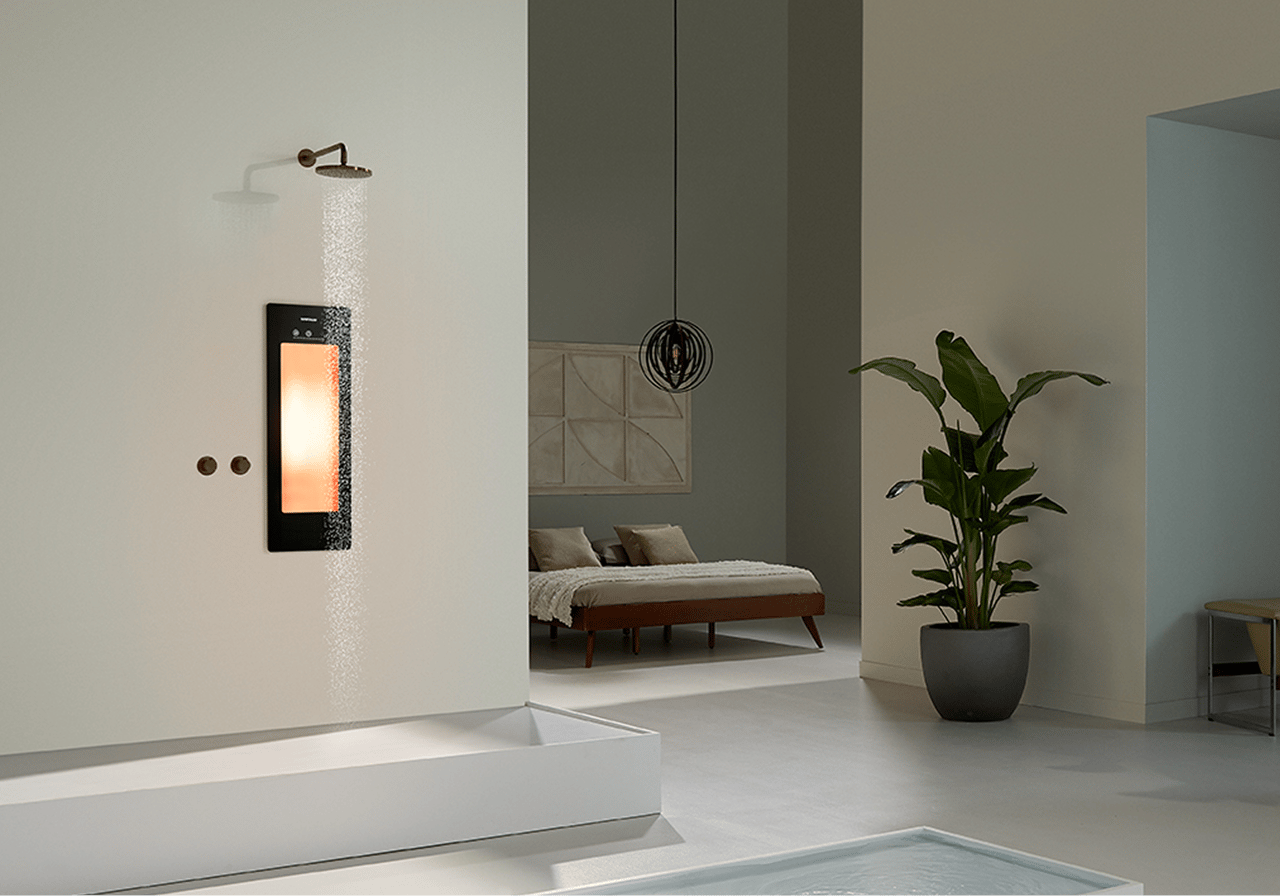 Ruime badkamer met een Sunshower-paneel dat warm licht geeft, ingebouwd in de douchewand. Naast de douche staat een grote groene plant en op de achtergrond een slaapkamer met een laag bed.