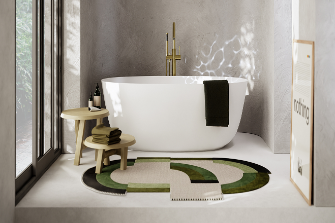 Lichte, moderne x²o badkamers setting met een vrijstaand wit bad, goudkleurige staande kraan en twee houten bijzettafels. Op de vloer ligt een opvallend rond vloerkleed in groen- en natuurtinten. Links zorgen grote ramen voor natuurlijk lichtinval, en rechts staat een ingekaderd kunstwerk.