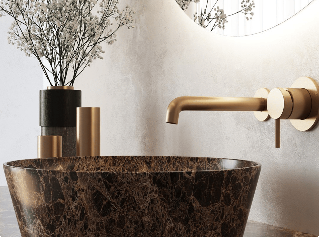 Detail van een luxueuze x²o badkamers wastafel in donkere marmerlook met een goudkleurige wandkraan. Links op het werkblad staan cilindervormige decorstukken in goud en zwart, met fijne witte bloemen op de achtergrond. Alles is gestyled in zachte, natuurlijke tinten.