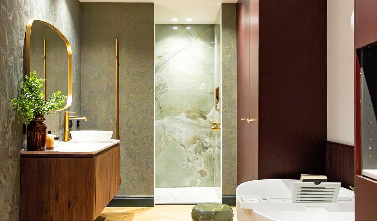 Auf diesem x²o badkamers Foto siehst du einen Überblick über das gesamte Ensuite-Badezimmer: links der Holz-Waschtisch mit Spiegel und Deko, rechts die begehbare Dusche mit grünem Marmor-Look, ein Schrank mit dunklen Paneelen und vorne eine moderne freistehende Badewanne.