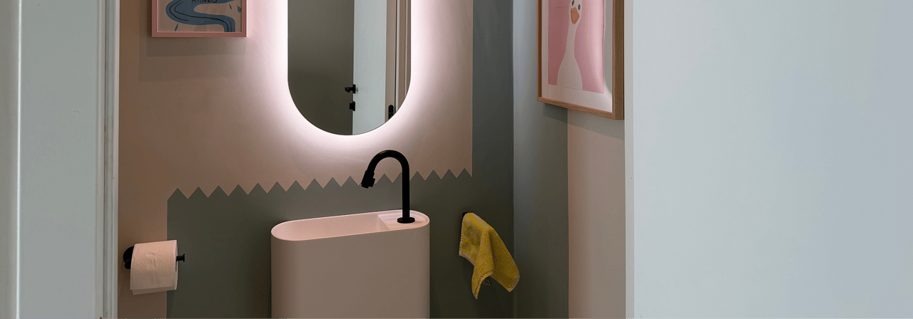 Detailansicht eines stilvollen Toilettenraums von x²o Badezimmer mit Balmani Livo Waschbecken, schwarzer Armatur und beleuchtetem Spiegel.
