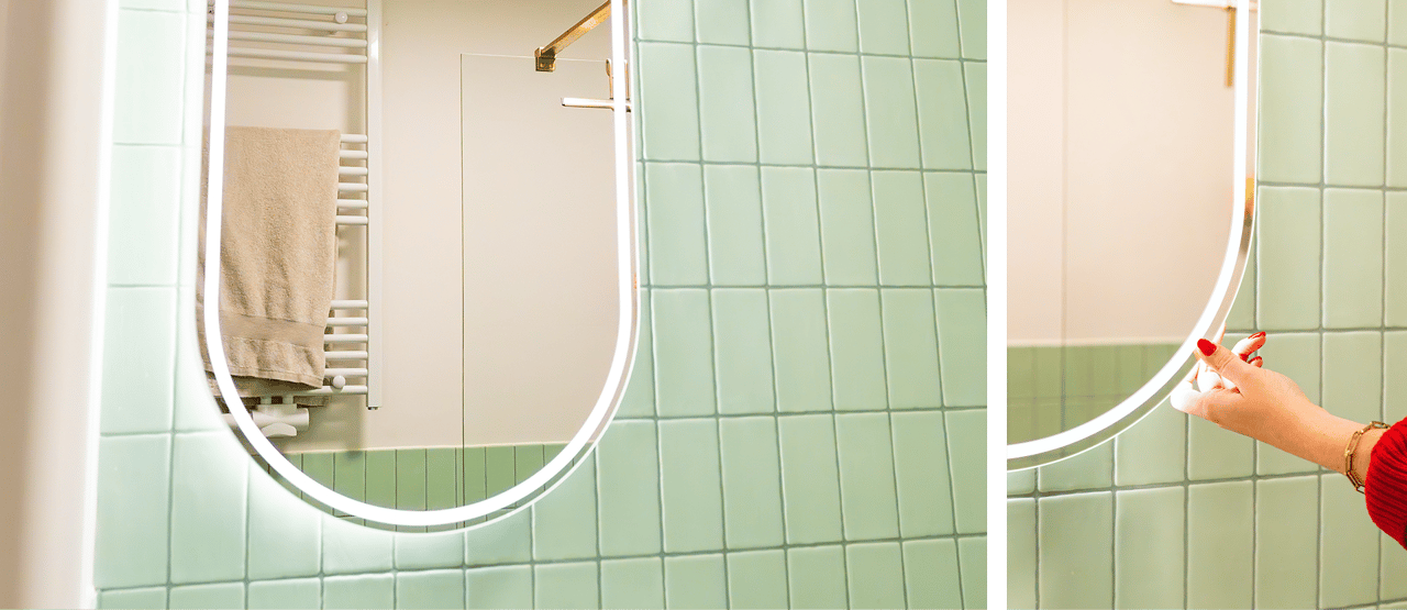 In diesem x²o Badezimmer siehst du einen ovalen Spiegel mit integrierter LED-Beleuchtung, die du mit einer Berührung aktivierst, im Hintergrund ein Handtuchheizkörper und grüne Wandfliesen.