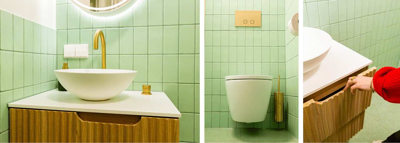 In diesem x²o Badezimmer siehst du links ein Aufsatzwaschbecken auf einem Holzmöbel mit goldener Armatur, in der Mitte ein wandhängendes WC mit goldener WC-Bürste und rechts eine Hand, die die Schublade des Möbels öffnet.