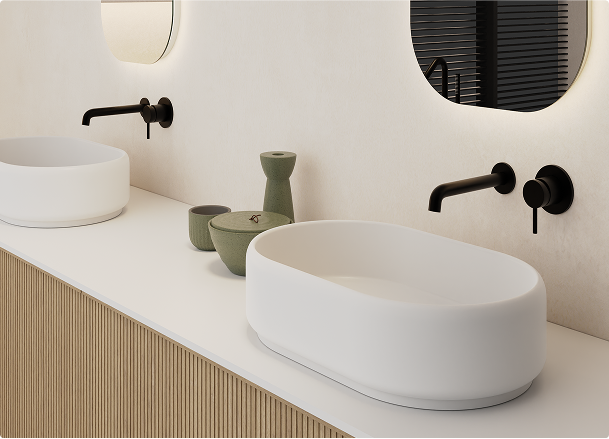 x²o badkamers met organische vormen, met ovale opzetwastafels, ronde spiegels met verlichting, zwarte muurkranen en accessoires in aardetinten op een houten onderkast.