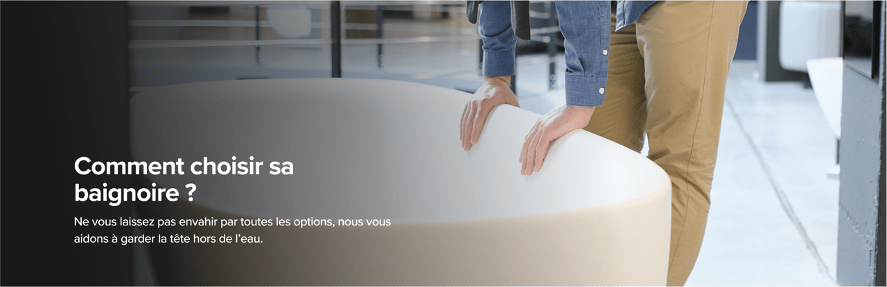 Sur cette image de x²o badkamers, un homme en pantalon beige et chemise bleue examine une grande baignoire design van x²o badkamers in een showroom met een industriële vloer en andere badmodellen op de achtergrond.