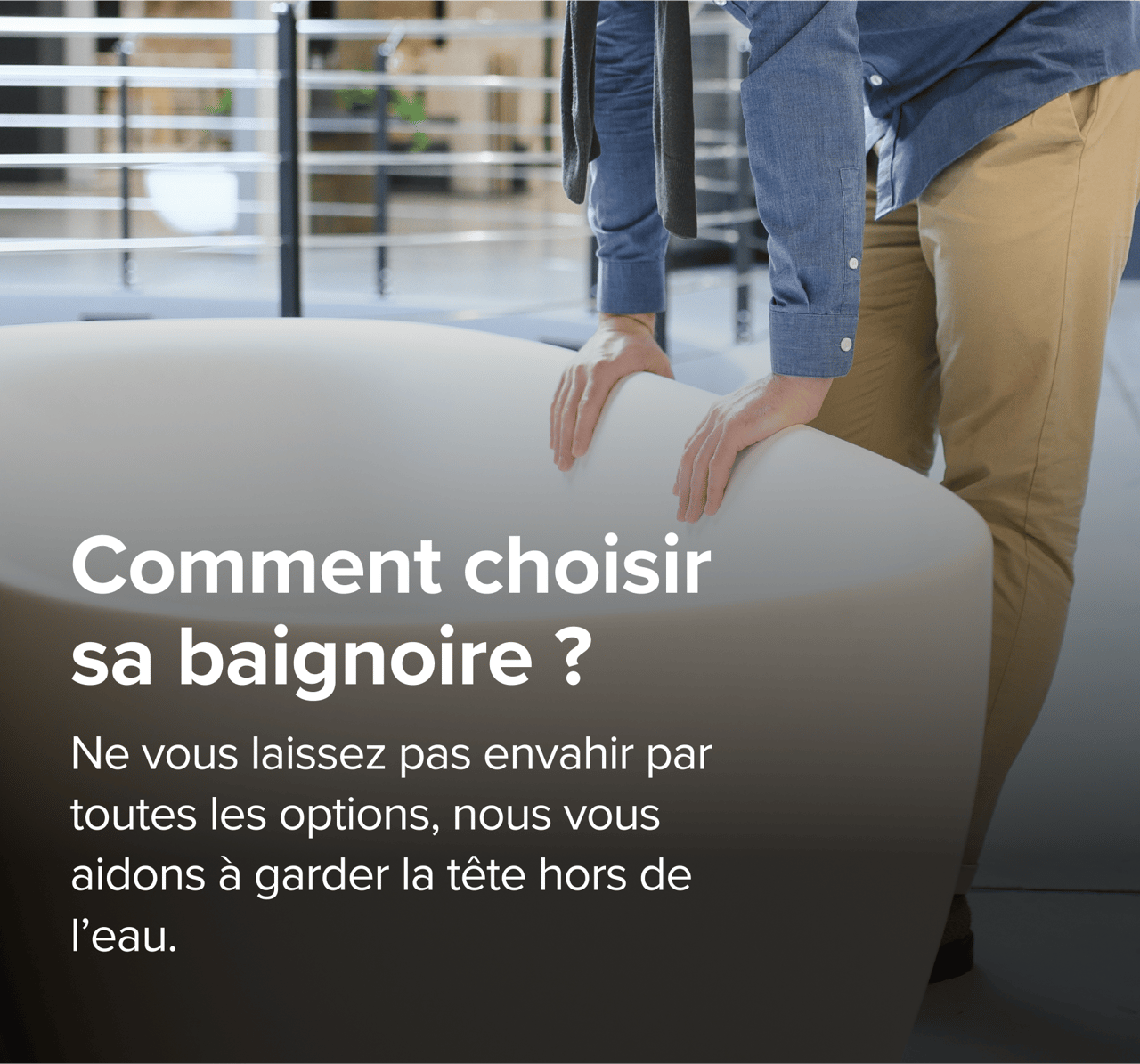 Sur cette image de x²o badkamers, un homme en pantalon beige et chemise bleue examine une grande baignoire design van x²o badkamers in een showroom met een industriële vloer en andere badmodellen op de achtergrond.