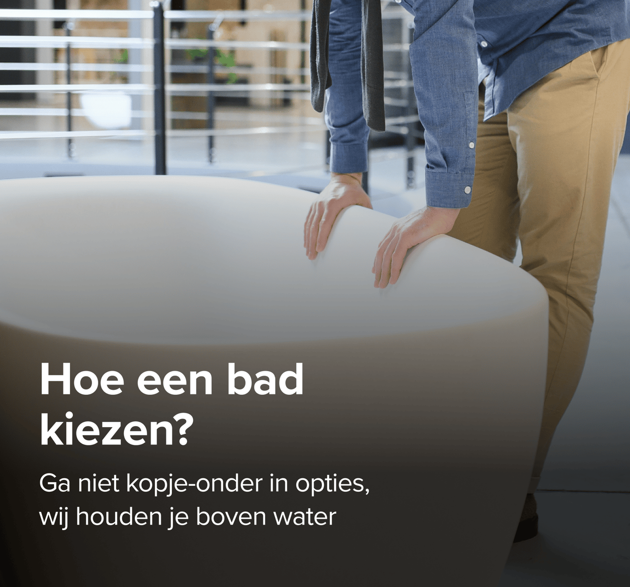 Op deze foto van x²o badkamers zie je een man in beige broek en blauwe blouse die een grote designbadkuip van x²o badkamers bekijkt in een showroom met een industriële vloer en andere badmodellen op de achtergrond.