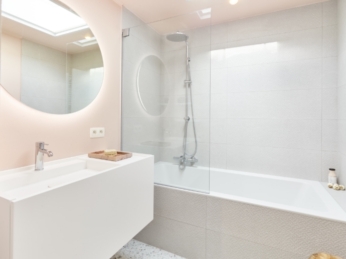 Bad met glazen douchewand, regendouche en wastafel met strakke, witte afwerking.