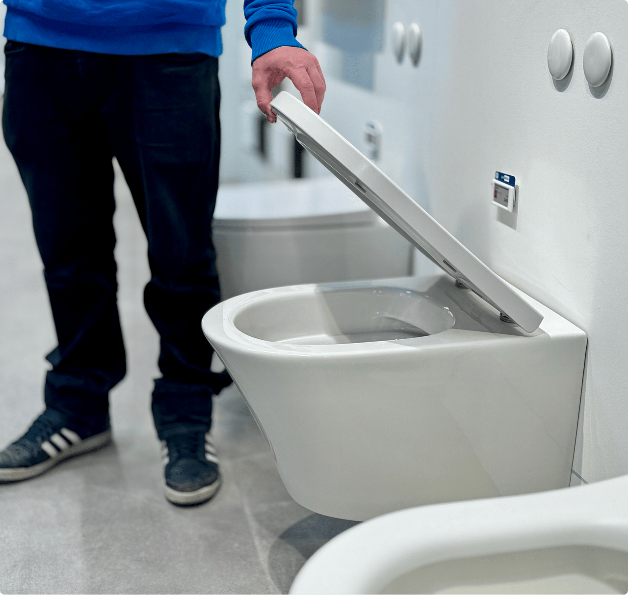 Een klant in blauwe trui test een toiletzitting in de showroom. Op de achtergrond staan andere toiletten. Interactieve beleving bij x²o badkamers.