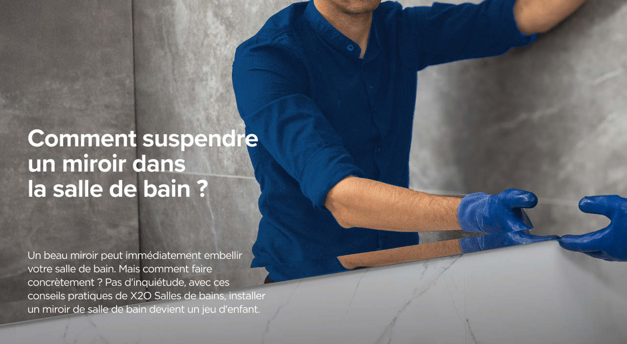 Installateur en tenue bleue fixant un miroir sur un mur de salle de bains effet marbre – un guide pratique de x²o salles de bains.