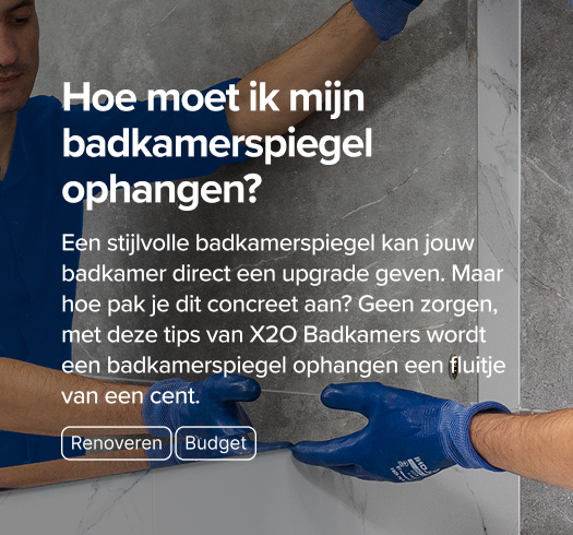 Monteur in blauwe werkkledij bevestigt een spiegel aan een badkamerwand met marmerlook – een praktische gids van x²o badkamers.