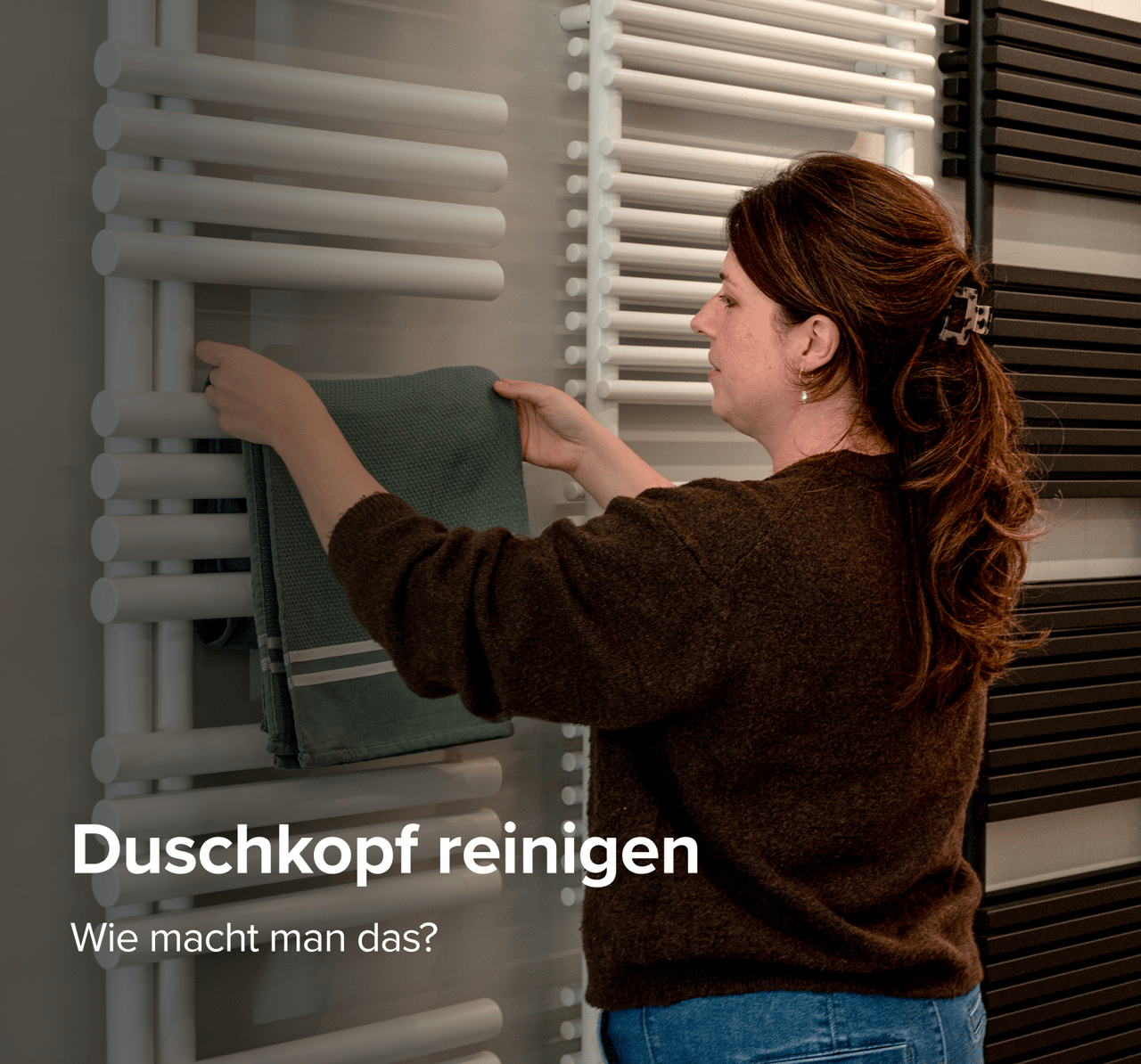 Frau hängt ein grünes Handtuch an einen weißen Heizkörper zwischen schwarzen Modellen im X2O badezimmer Showroom.”