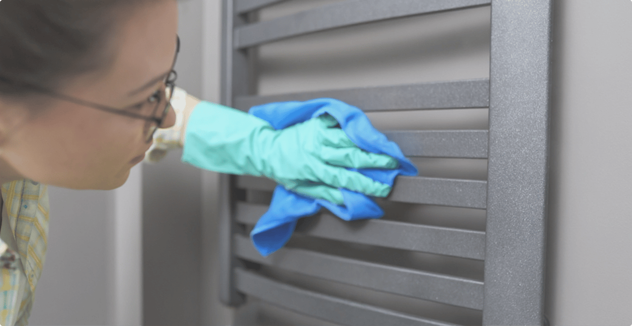 Vrouw met handschoenen poetst een grijze handdoekradiator zorgvuldig schoon in een X2O badkamers interieur.