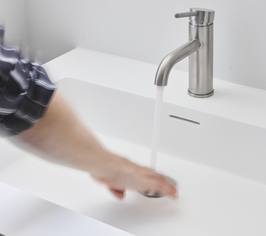 Detail eines Edelstahl-Wasserhahns auf einem weißen Waschbecken.