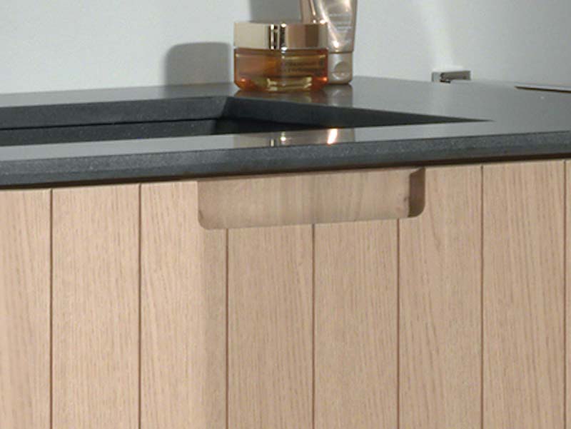 Detail van een houten wastafelmeubel met een donkergrijs blad en een subtiele metalen ladegreep.