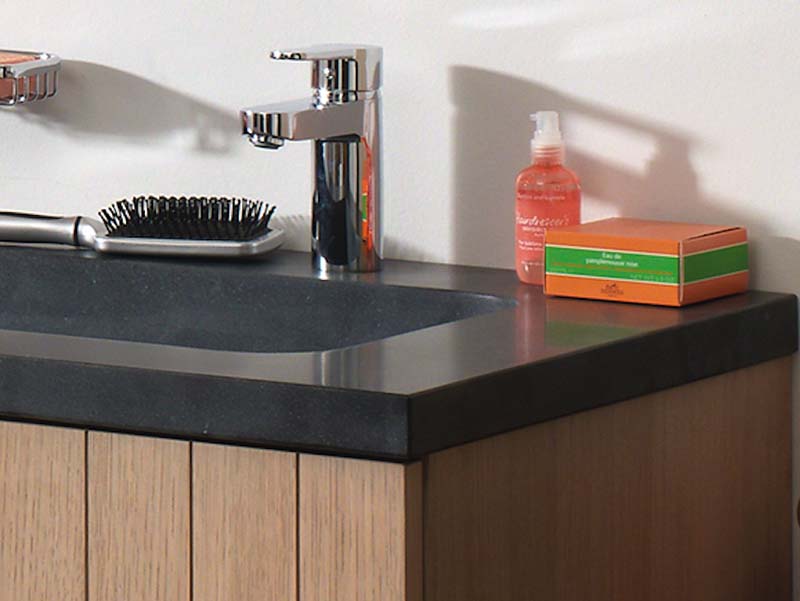 Houten wastafelmeubel met donker stenen blad, geïntegreerde wastafel, chromen kraan en accessoires.