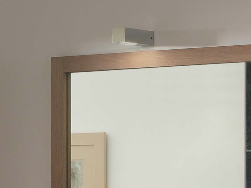 Detail van een spiegel met houten frame en geïntegreerde bovenverlichting in een modern design.