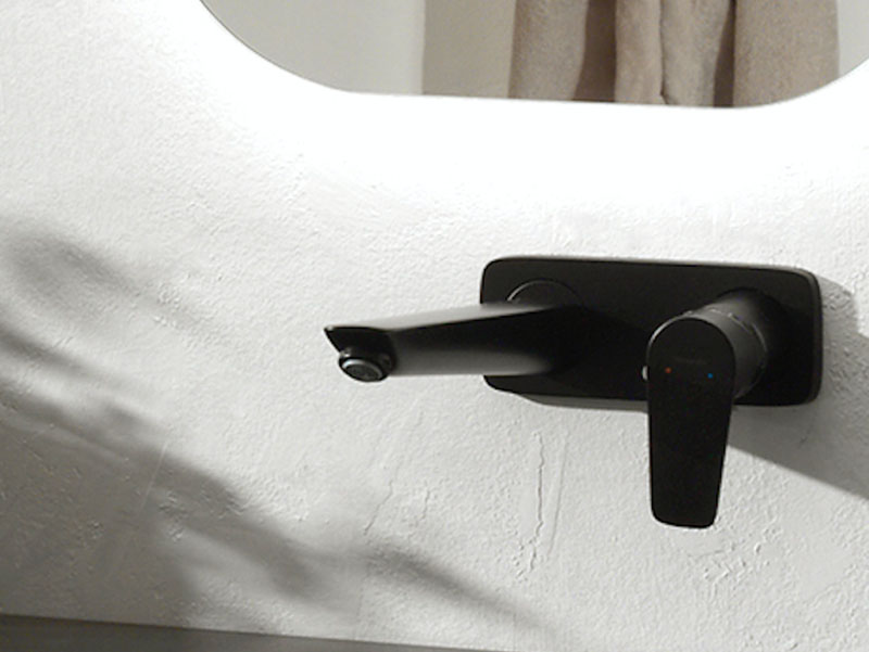 Detail van een zwarte wandkraan met modern ontwerp, bevestigd aan een witte muur.