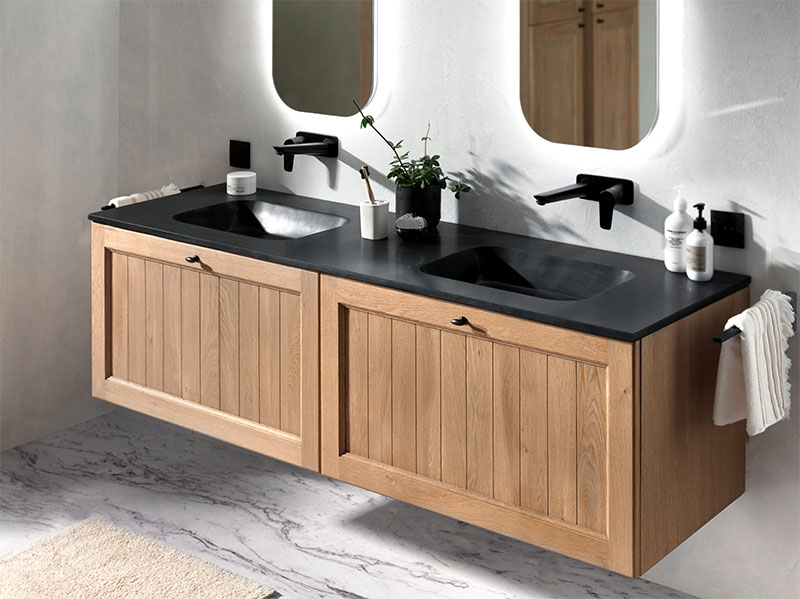Dubbele wastafel met houten onderkasten, donker stenen blad, zwarte kranen en verlichte spiegels.