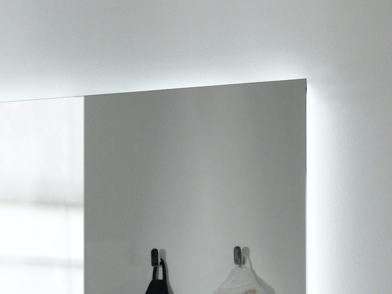 Detail van een verlichte spiegel met een strak, minimalistisch ontwerp en handdoekhaken ernaast.