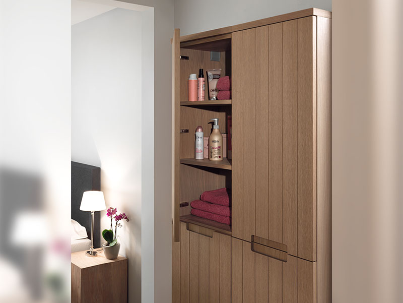 Detail van een houten badkamerkast met open deur, gevuld met handdoeken en verzorgingsproducten.