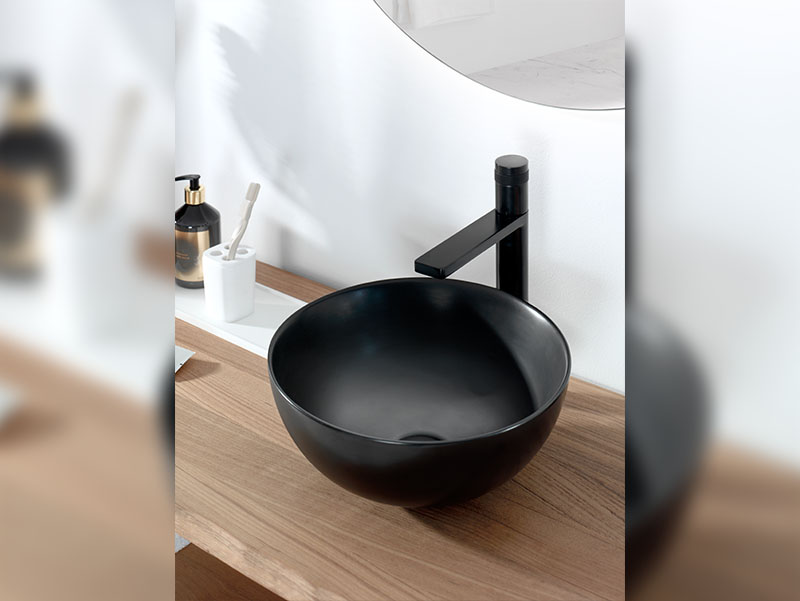 Zwarte opzetwaskom op houten badkamermeubel met bijpassende zwarte kraan en ronde spiegel.