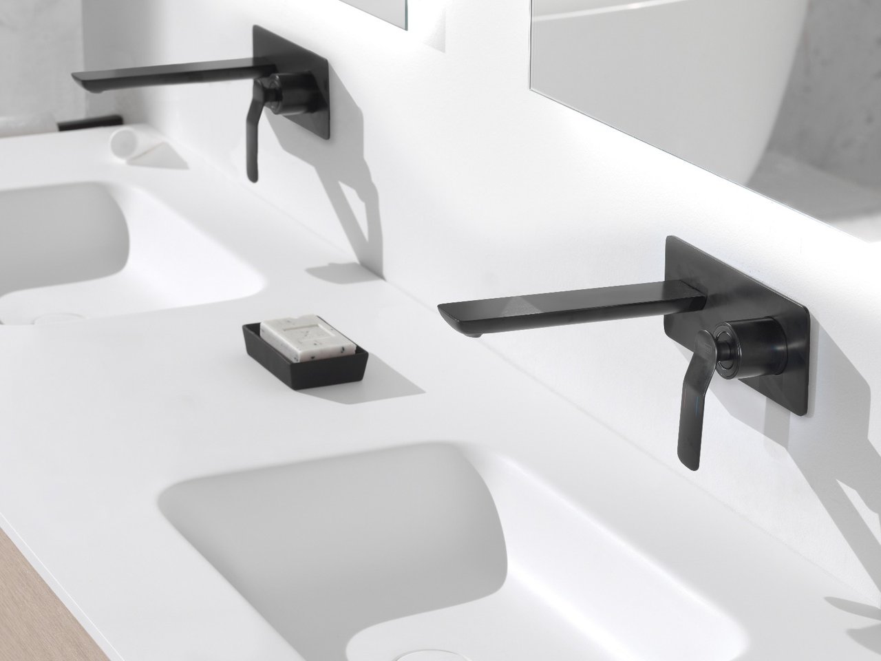 Witte wastafel met twee zwarte wandkranen en geïntegreerde spoelbakken.