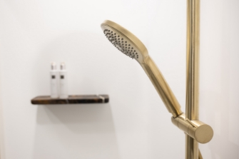 Luxe douche met gouden handdouche en marmeren plank tegen een witte wand voor een elegante uitstraling.