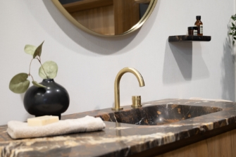 Luxe wastafel met donker marmeren blad, gouden kraan en ronde spiegel voor een elegante uitstraling