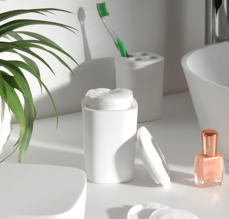 Witte container voor watjes, groene tandenborstel, nagellak en plantje.