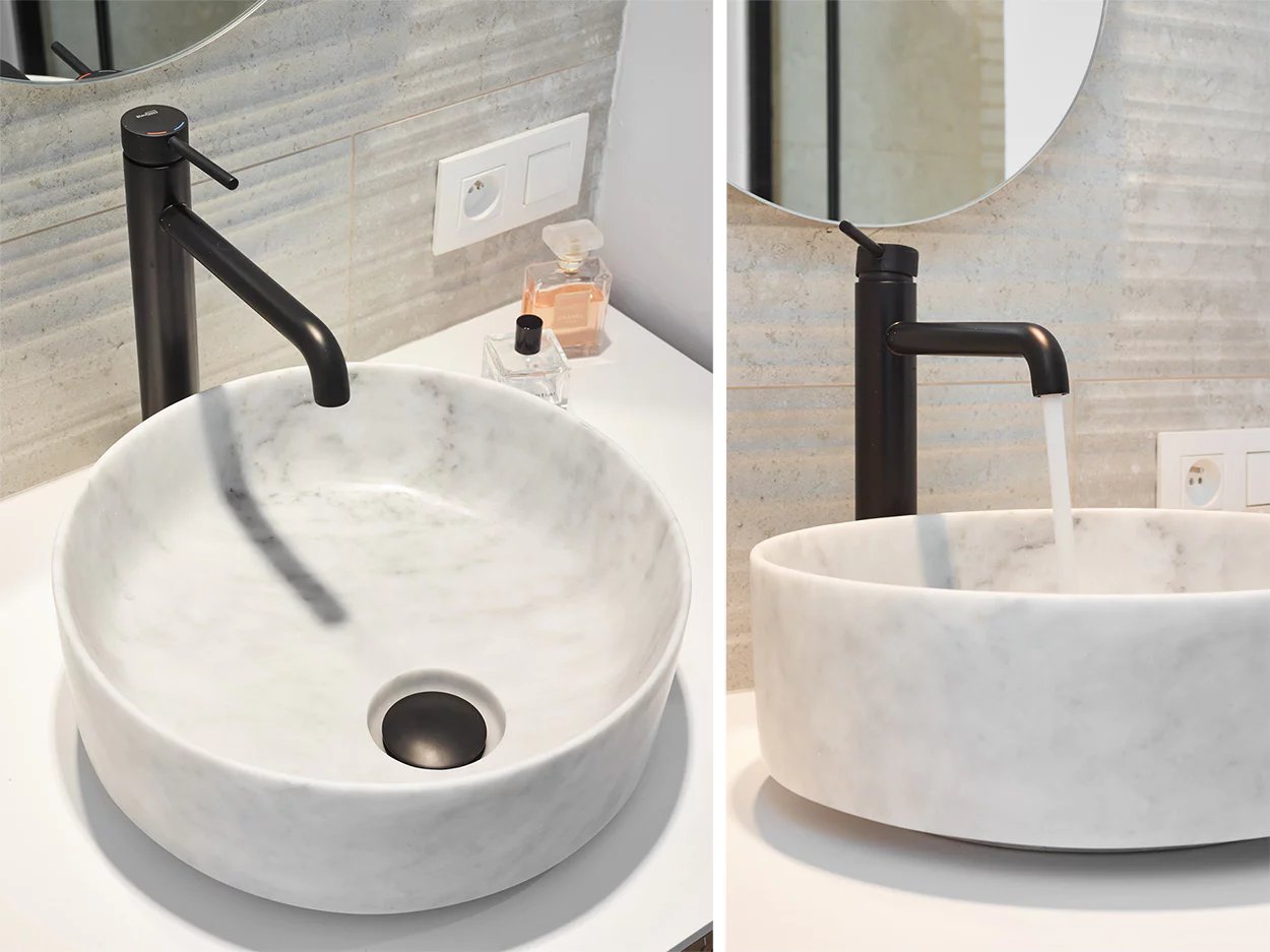 Lavabo en marbre avec robinet noir et jet d'eau.