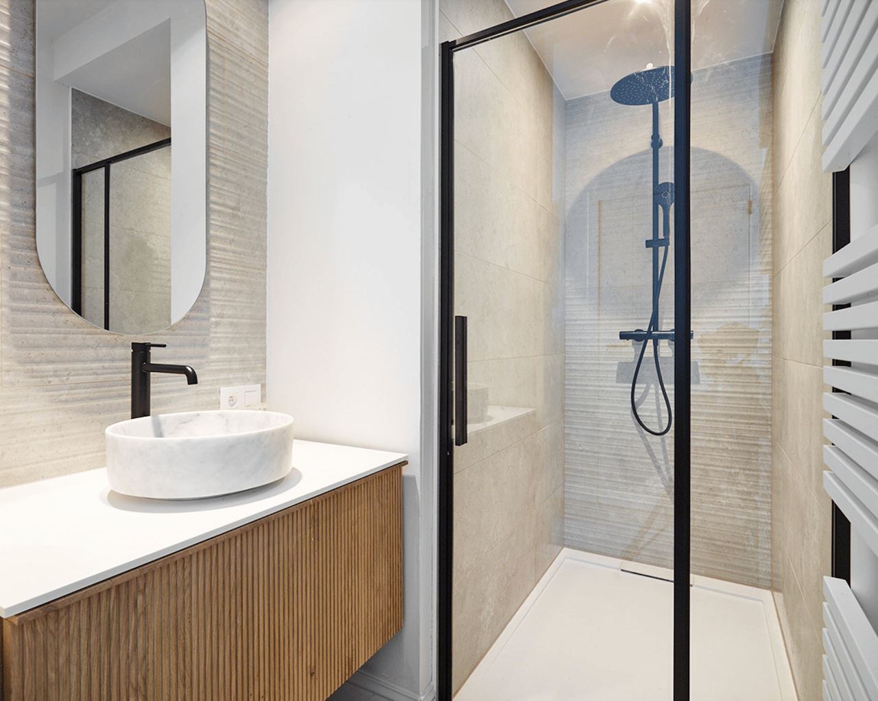 Lavabo en marbre sur meuble en bois, robinet noir, cabine de douche en verre avec douche à pluie et radiateur.