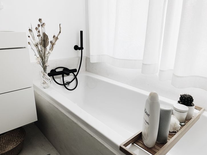 Moderne Badezimmer mit weißer Badewanne, schwarzem Wasserhahn und Pflegeprodukten