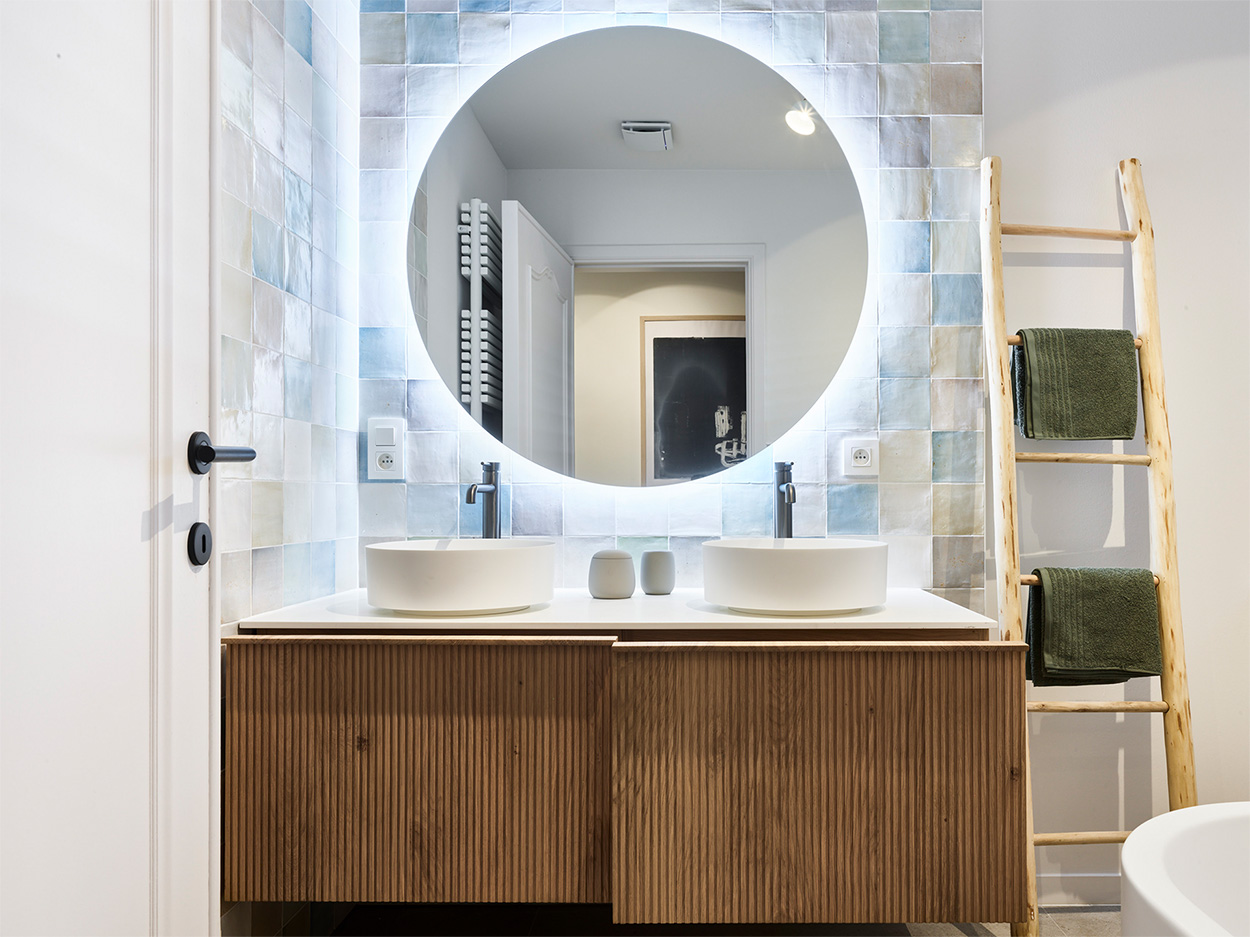 Modernes Badezimmer mit Doppelwaschbecken, rundem Spiegel und Handtüchern auf Leiterregal