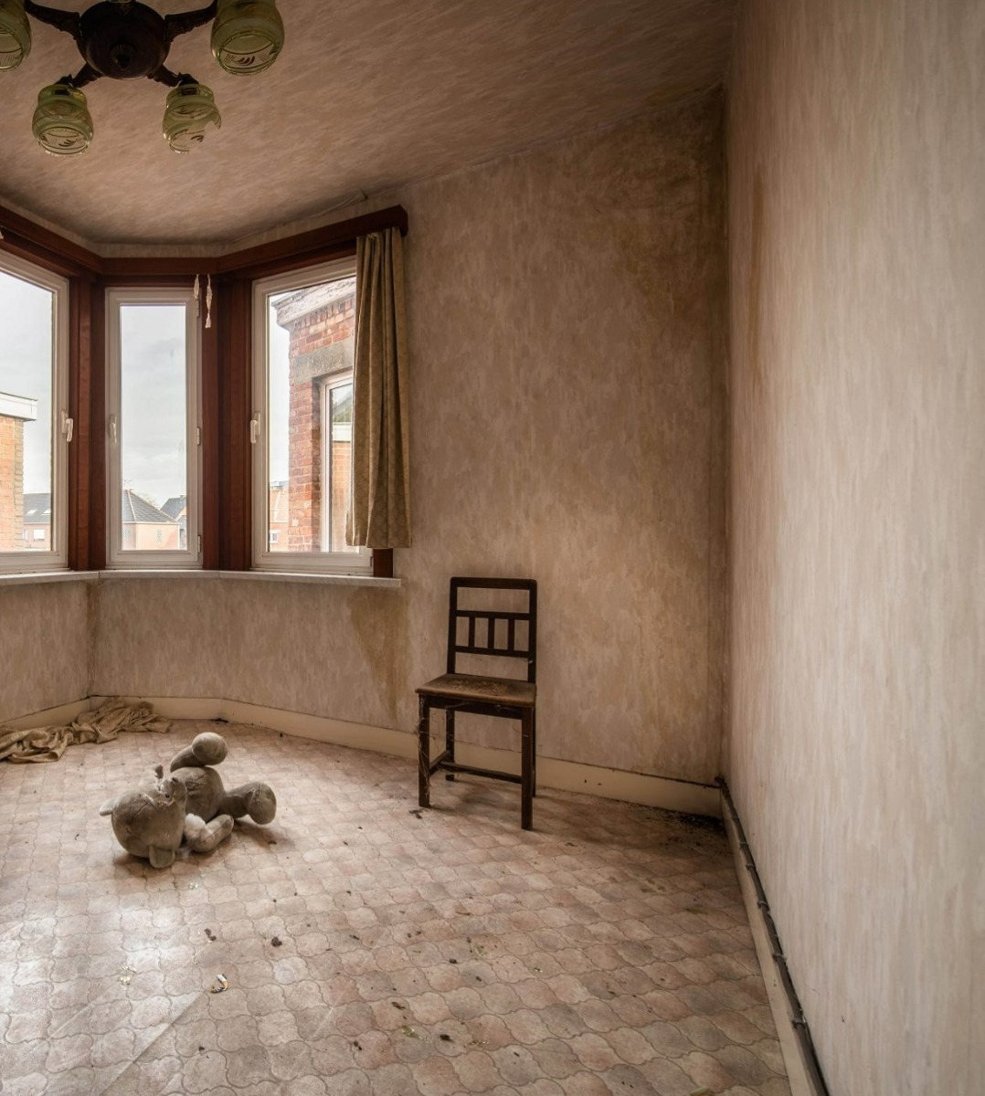 Verwaarloosde kamer met houten stoel, teddybeer op de vloer en verouderde muren