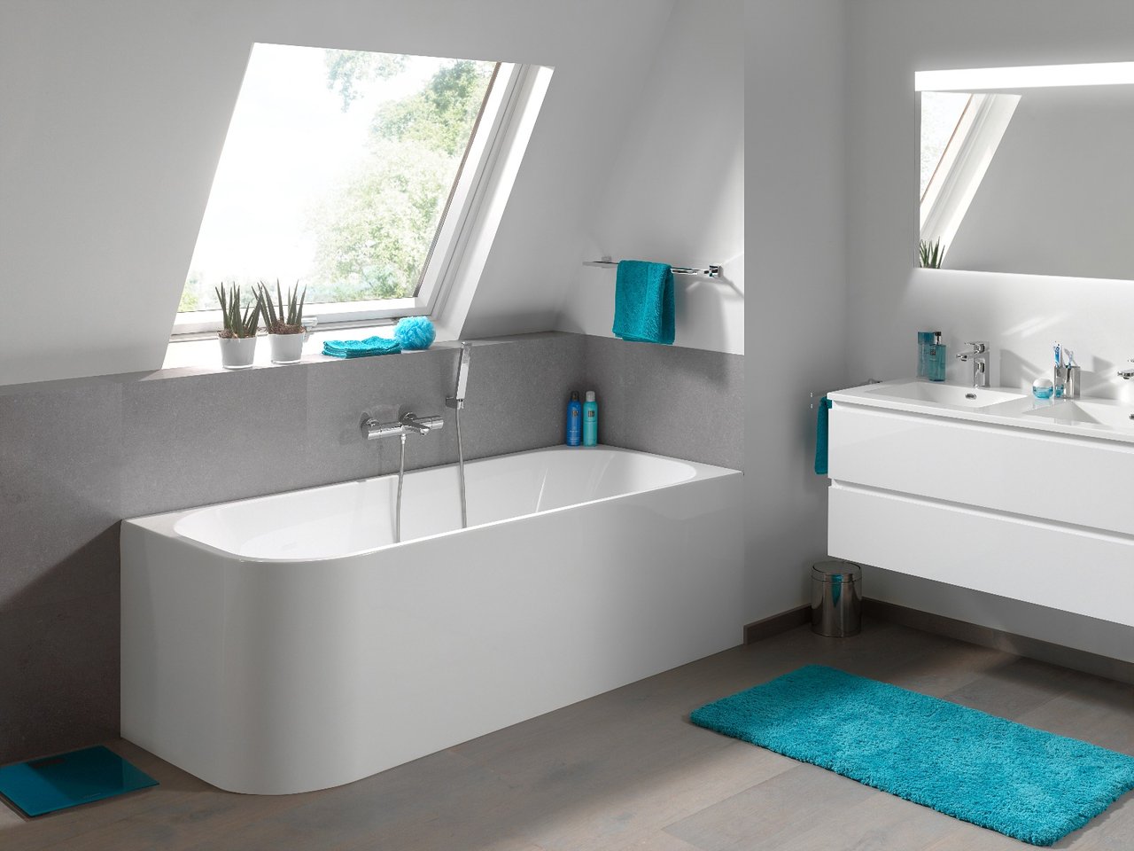 Salle de bains moderne avec baignoire indépendante, double lavabo, accessoires turquoise et fenêtre de toit inclinée