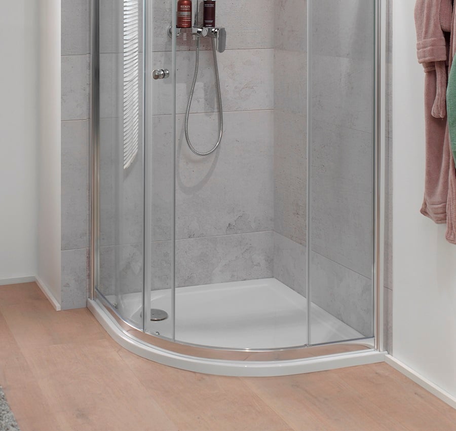 Cabine de douche avec porte en verre incurvée, carreaux gris, pommeau de douche et accessoires au mur, serviettes accrochées sur le côté