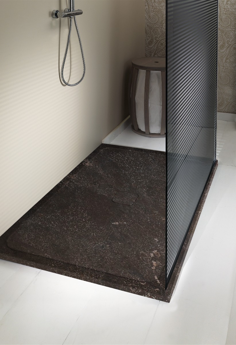 Douche moderne avec un sol en pierre brun foncé et une paroi vitrée. Il y a un drain caché et une petite chaise rayée gris/blanc