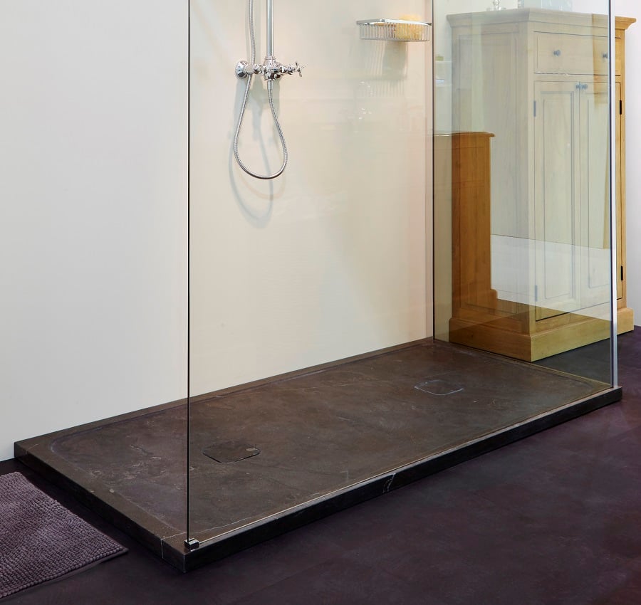 Douche moderne avec un sol en pierre sombre, une paroi vitrée et un panier de rangement pour accessoires de salle de bain. Le sol a un drain minimaliste