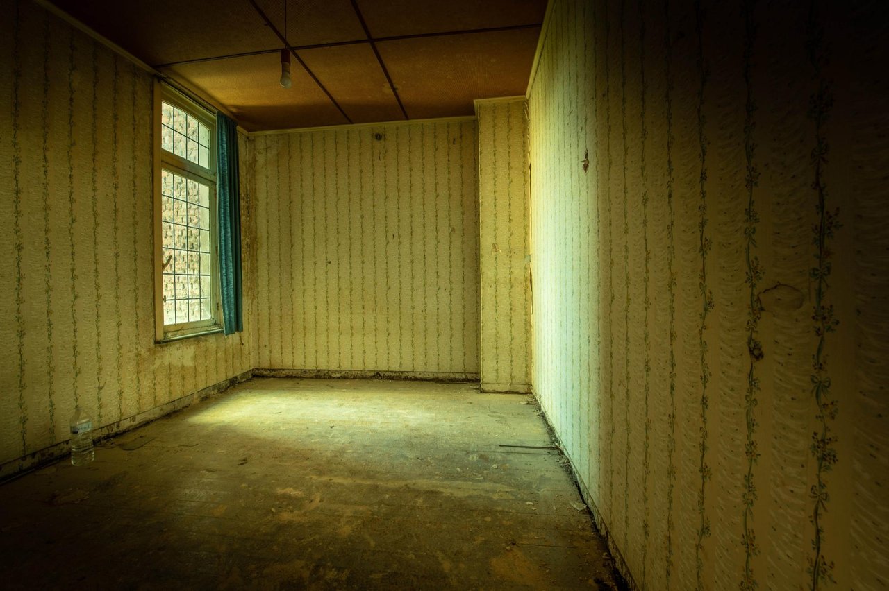 Leerer Raum mit veraltetem Tapeten, Holzfußboden und blauen Vorhängen im Fenster, schafft eine verlassene Atmosphäre