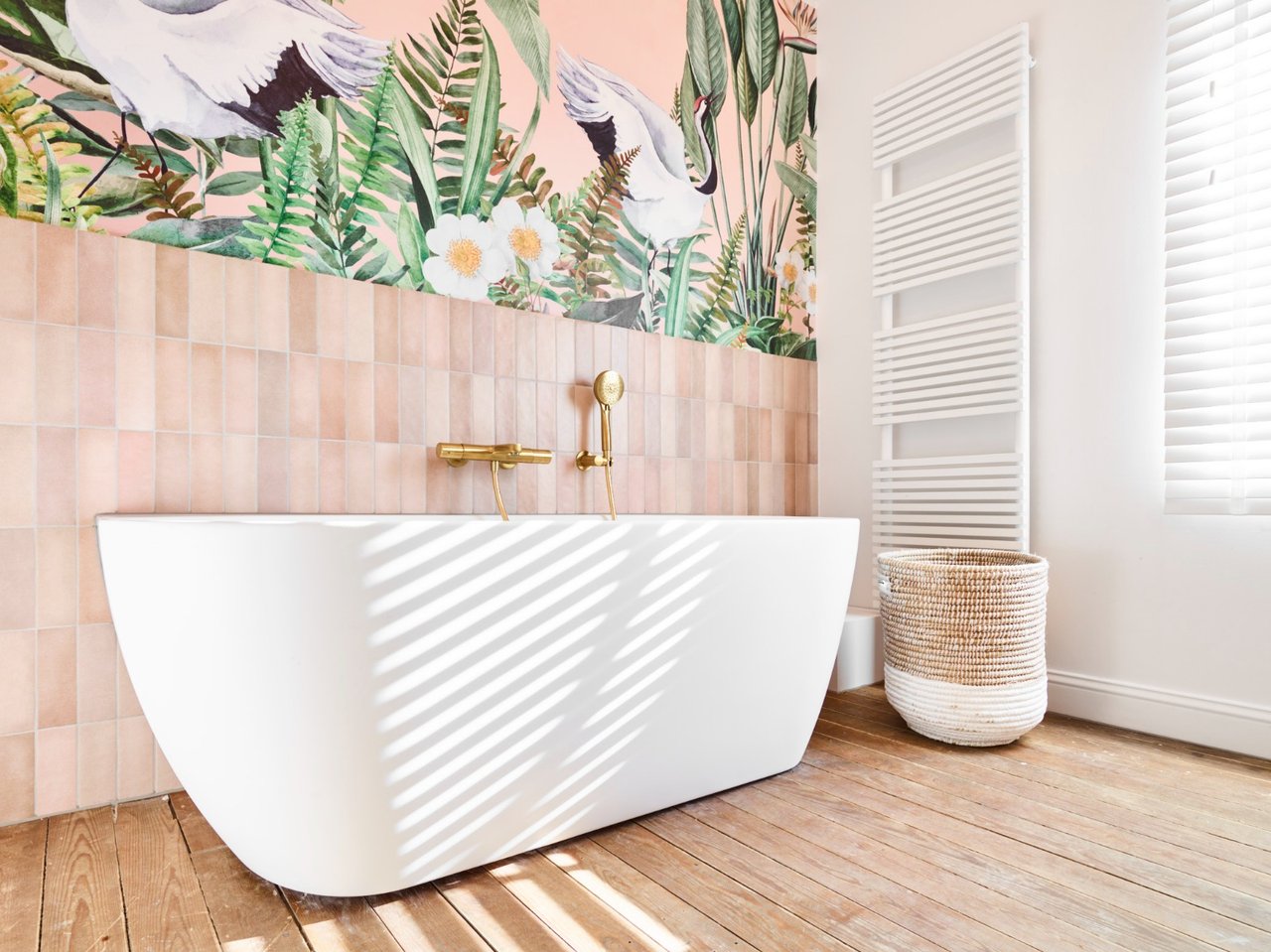 Moderne badkamer met een witte badkuip, gouden kranen en tropisch muurschildering van roze tinten met bloemen en vogels