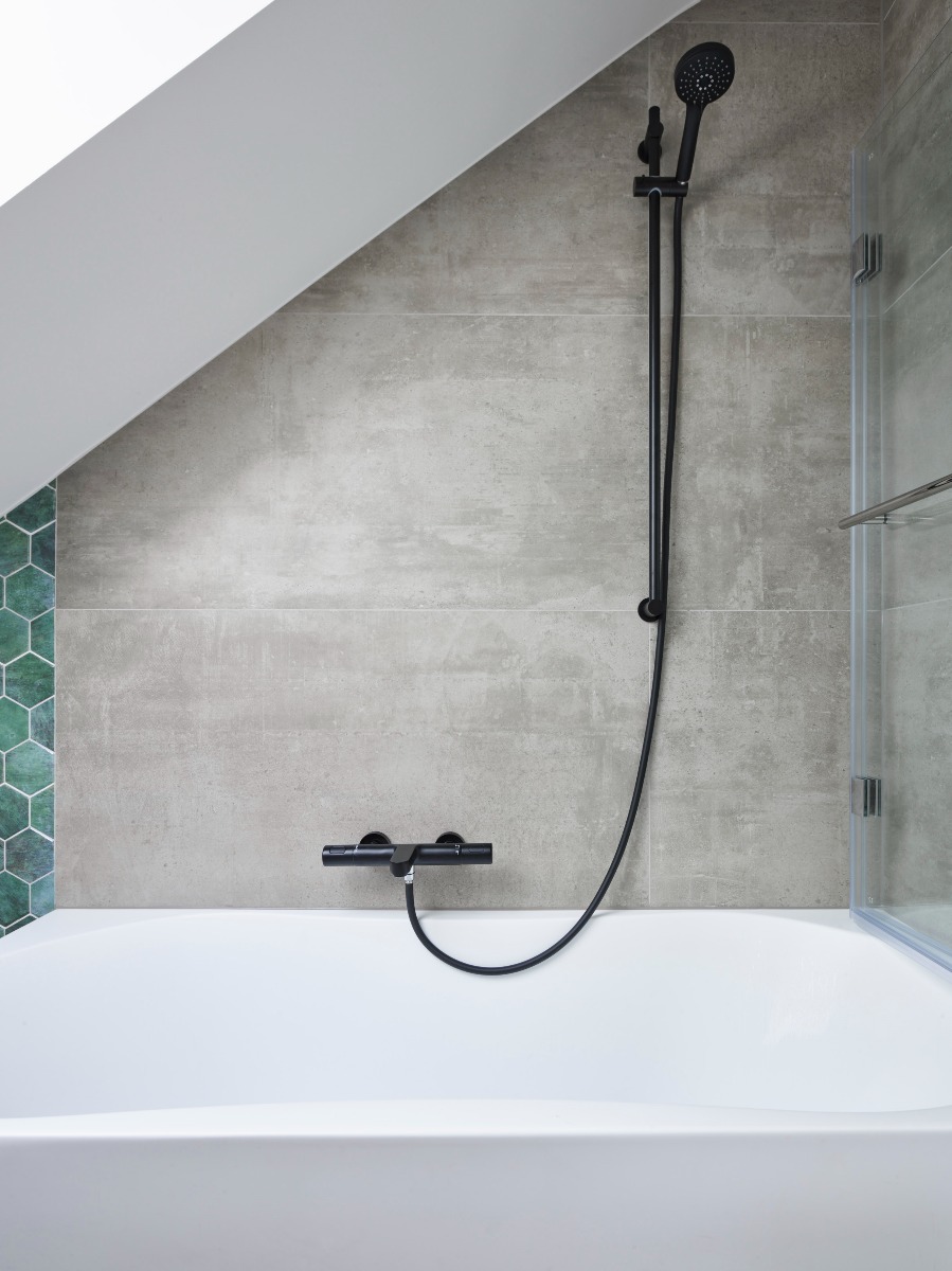 Badkamer met een vrijstaand bad, zwarte regendouche en groene hexagon tegels.