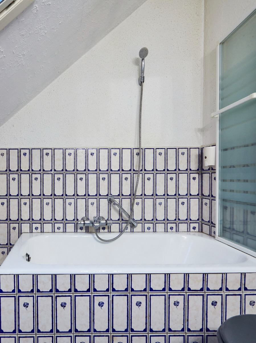 Bad met een douchezuil en klassieke kranen, omgeven door blauwe tegelwanden met bloemenmotief.