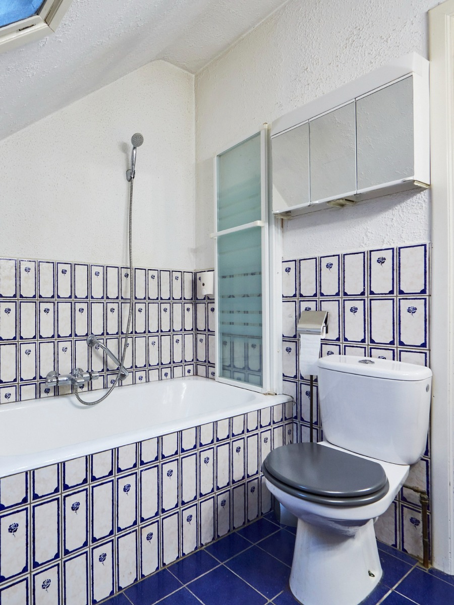 Bad met een douchezuil en een toilet, omgeven door blauwe tegelwanden met bloemenmotief.